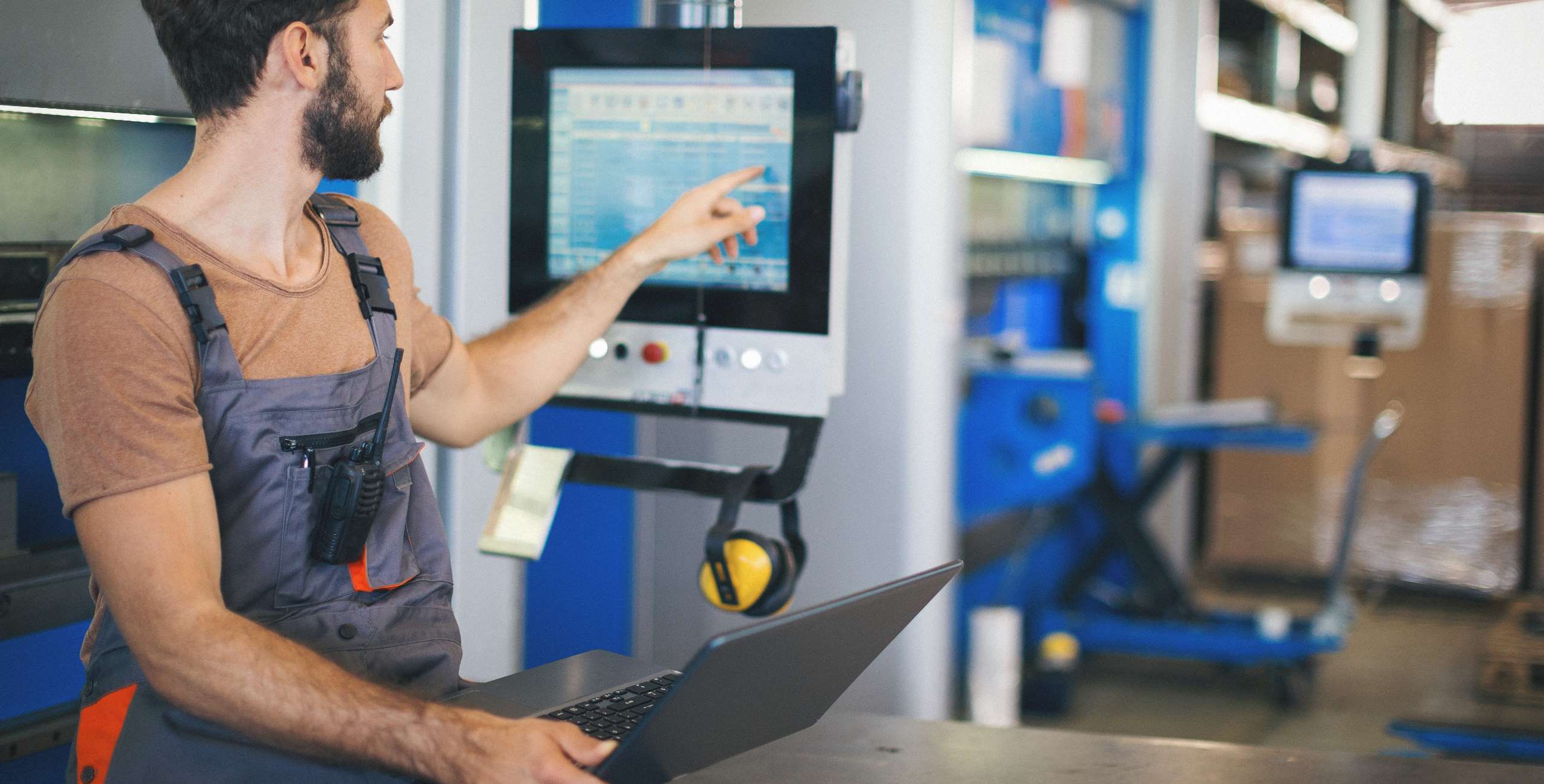 Operator werkt met een laptop en digitaal machinescherm in de productiehal.